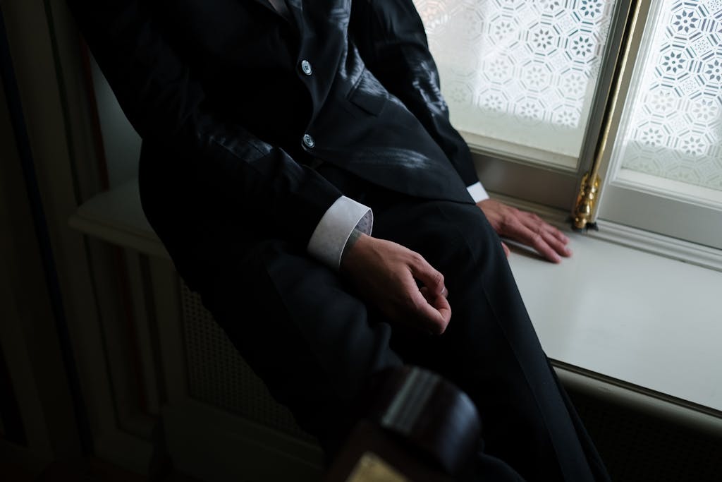 Close-up shot of a man in a black suit sitting by a window, showcasing sophistication.